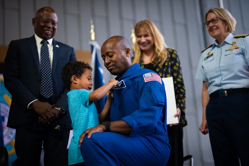 A person kneels down so a child can pin something to their lapel. People standing in the background smile.