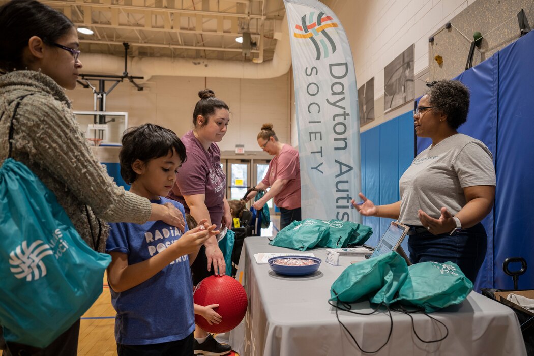 A woman talks to families at an information booth in a school gymnasium.