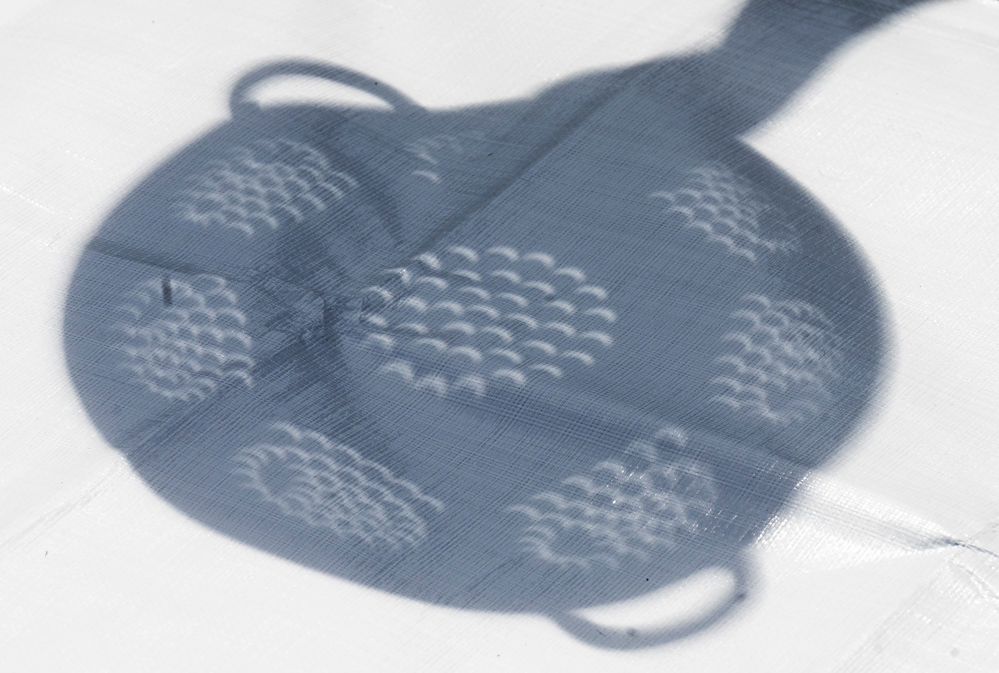 The shadow of a colander with a white background. The holes of the colander are all in a crescent shape.