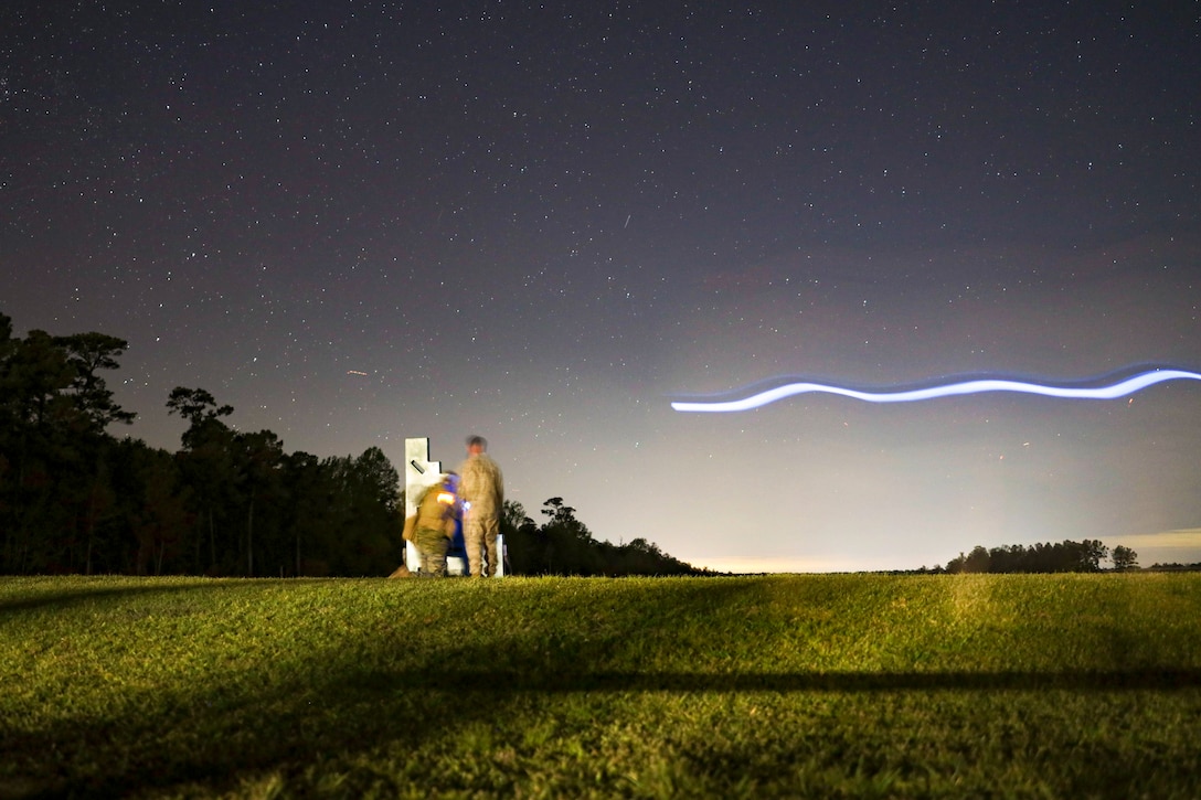 A blue streak moves toward two Marines as they stand and kneel in a field under a starry sky.