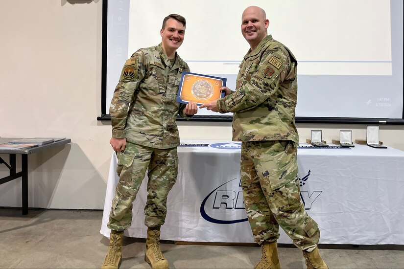 Two service members pose for a picture holding an award certificate.