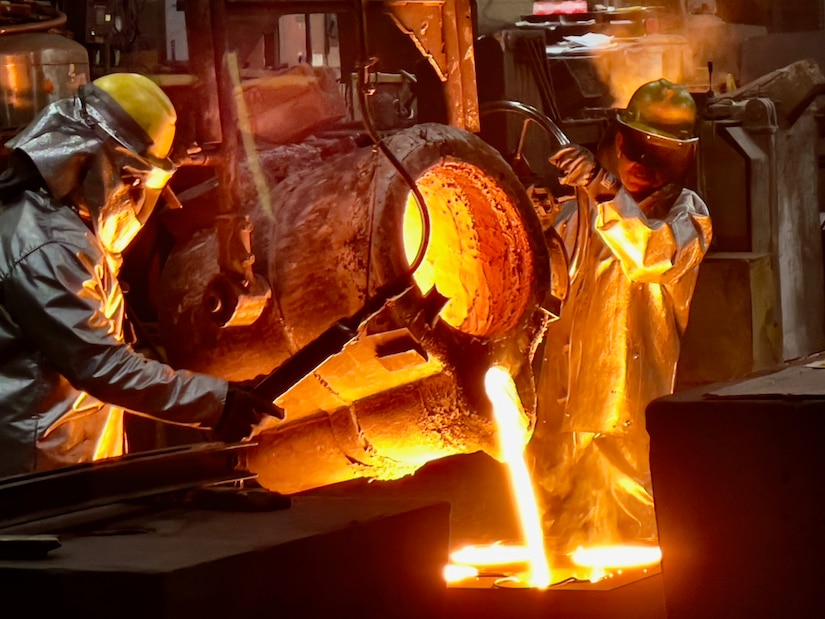 Two people pour a cauldron of molten metal into molds.