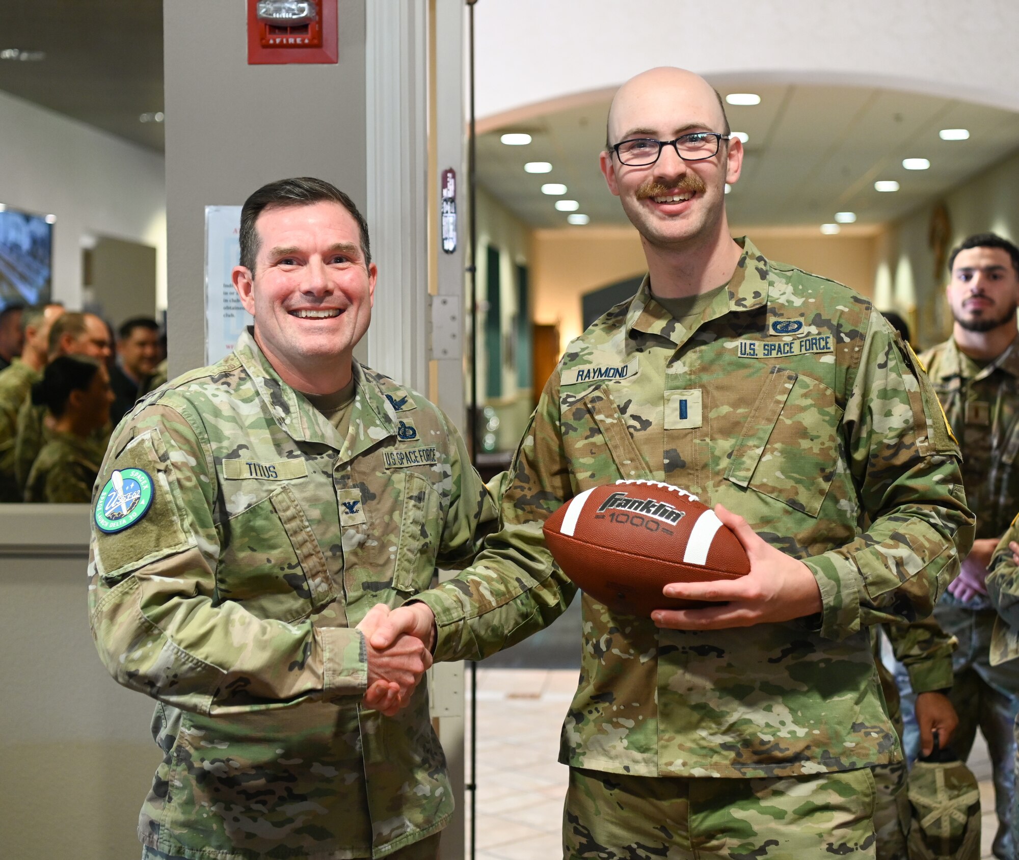 A Space Launch Delta 30 vice commander hands a 2nd Space Launch Squadron Responsible engineer the game ball during a patching ceremony for USSF-62 at Vandenberg Space Force Base.