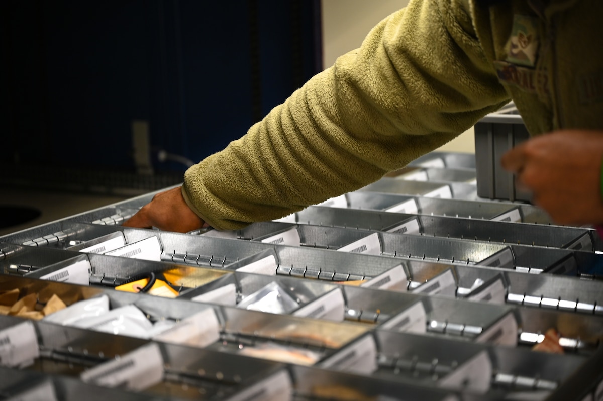 A military member puts their hand in a bin.