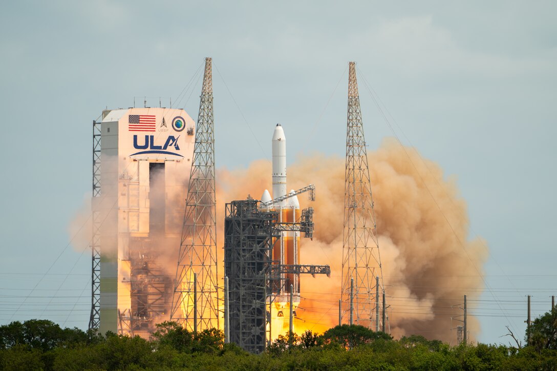 A rocket launches into the sky from a tower with the United States flag.