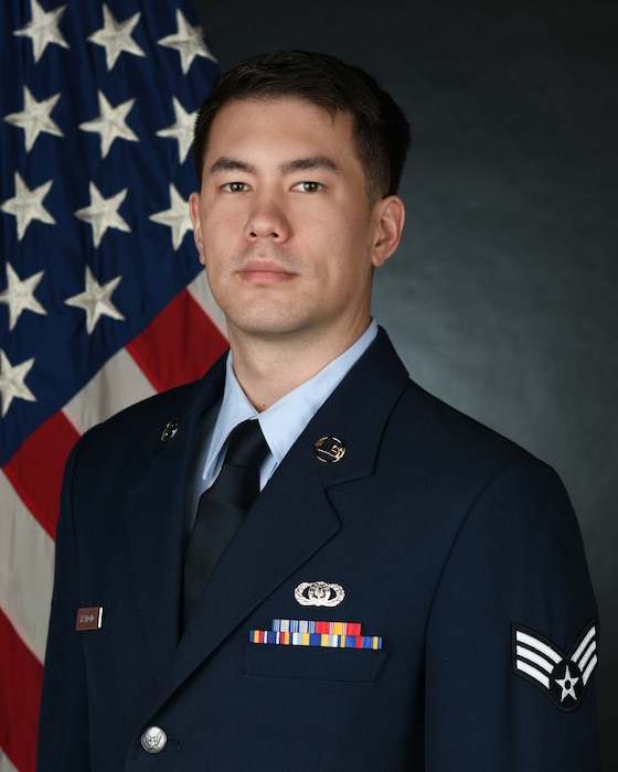 Official Photo of SrA Kai Hammond, saxophone.  SrA Hammond is wearing blue service dress and standing in front of an American flag.