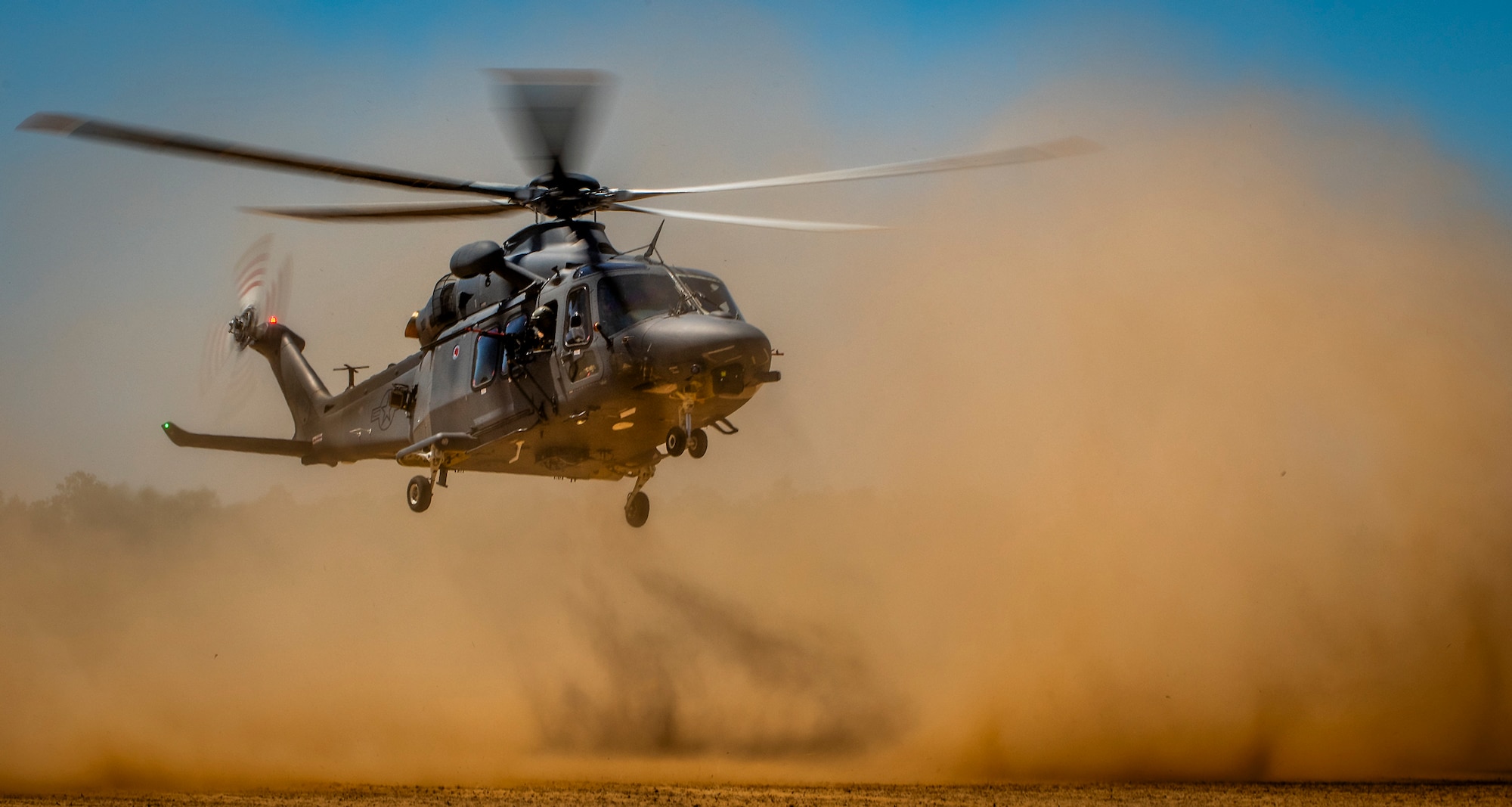 An MH-139A Grey Wolf lands on a soft dirt field
