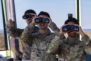(From left) U.S. Air Force Senior Airman Jantzen Scott, 6th Operation Support Squadron air traffic control trainer, Staff Sgt. Christian Traynor, a 6th OSS ATC watch supervisor, and Airman 1st Class Raymond Quichocho Jr, a 6th OSS ATC apprentice,  look at the flightline through binoculars at MacDill Air Force Base, Florida, April. 8, 2024.