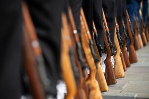 The brown rifles of dozens of honor guardsmen are resting on the ground next to each service member during a ceremony.