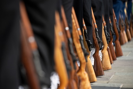 The brown rifles of dozens of honor guardsmen are resting on the ground next to each service member during a ceremony.
