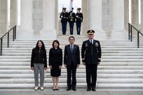 Four people are posing for a picture on white marble steps. At the top of the steps, two Army Soldiers are holding rifles on either side of another Soldier who is holding the Japanese flag.