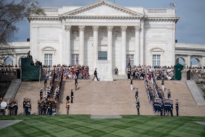 View of the steps up to the back side of the white marble Tomb of the Unknown Soldier and the building behind it that houses the history museum for the Tomb. There are various military members from each branch lining the steps.