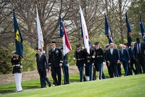 Military members hold various flags lining a walkway as other soldiers and civilians walk past.
