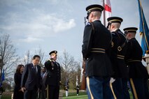 Three Army soldiers are presenting the colors, which includes the US and Japanese flags, while another soldier facing them salutes and another man bows.