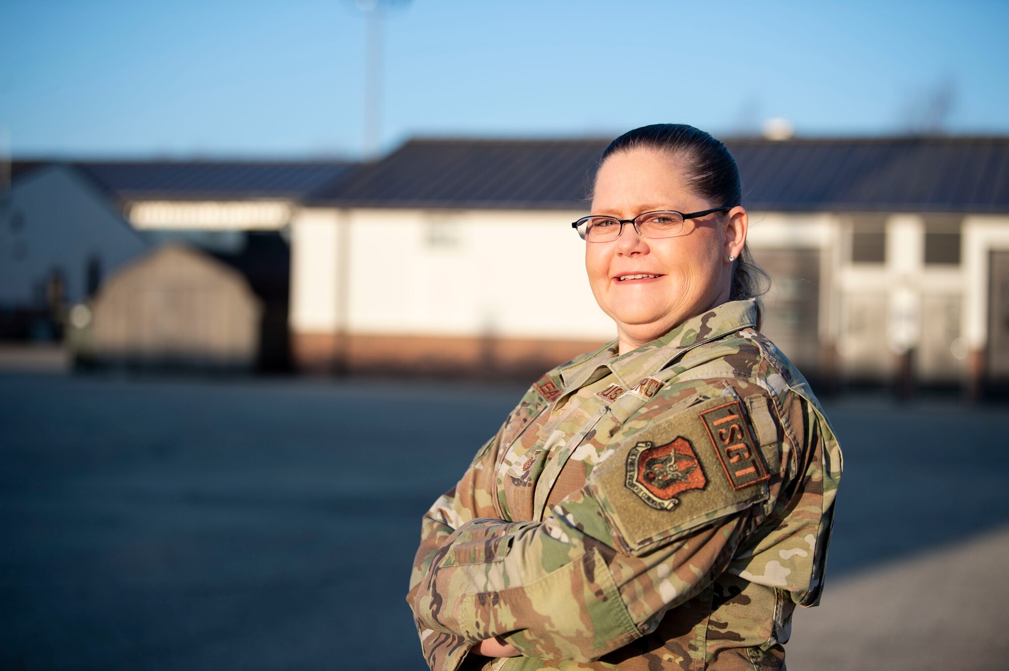 A woman in a U.S. Air Force uniform poses for a photo. In the background, blurred buildings.