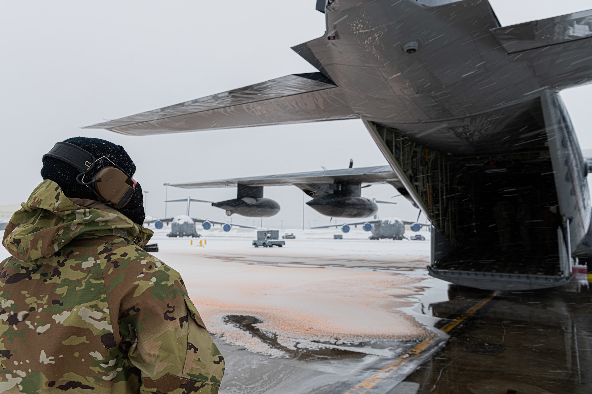 A person in military uniform looks at a parked military aircraft.