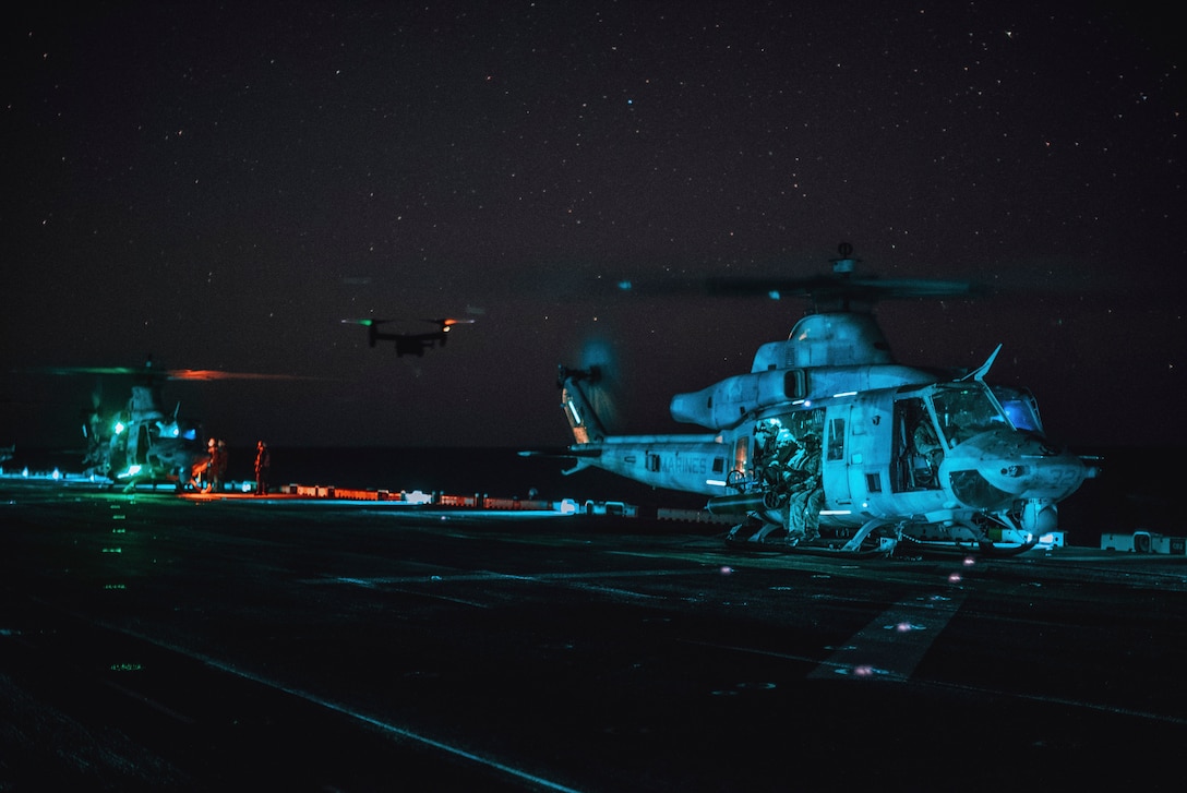 U.S. Marine Corps UH-1Y Venoms attached to Medium Tiltrotor Squadron (VMM) 165 (Reinforced), 15th Marine Expeditionary Unit, prepare for take-off while an MV-22B Osprey flies toward the amphibious assault ship USS Boxer (LHD 4) in the Pacific Ocean April 6, 2024. The Venoms conducted a helicopter insert for Marines assigned to Reconnaissance Company, 15th MEU, performing a reconnaissance and surveillance mission for a raid exercise ashore. Elements of the 15th MEU are currently embarked aboard the Boxer Amphibious Ready Group conducting routine operations in U.S. 3rd Fleet. (U.S. Marine Corps photo by Cpl.  Helms)