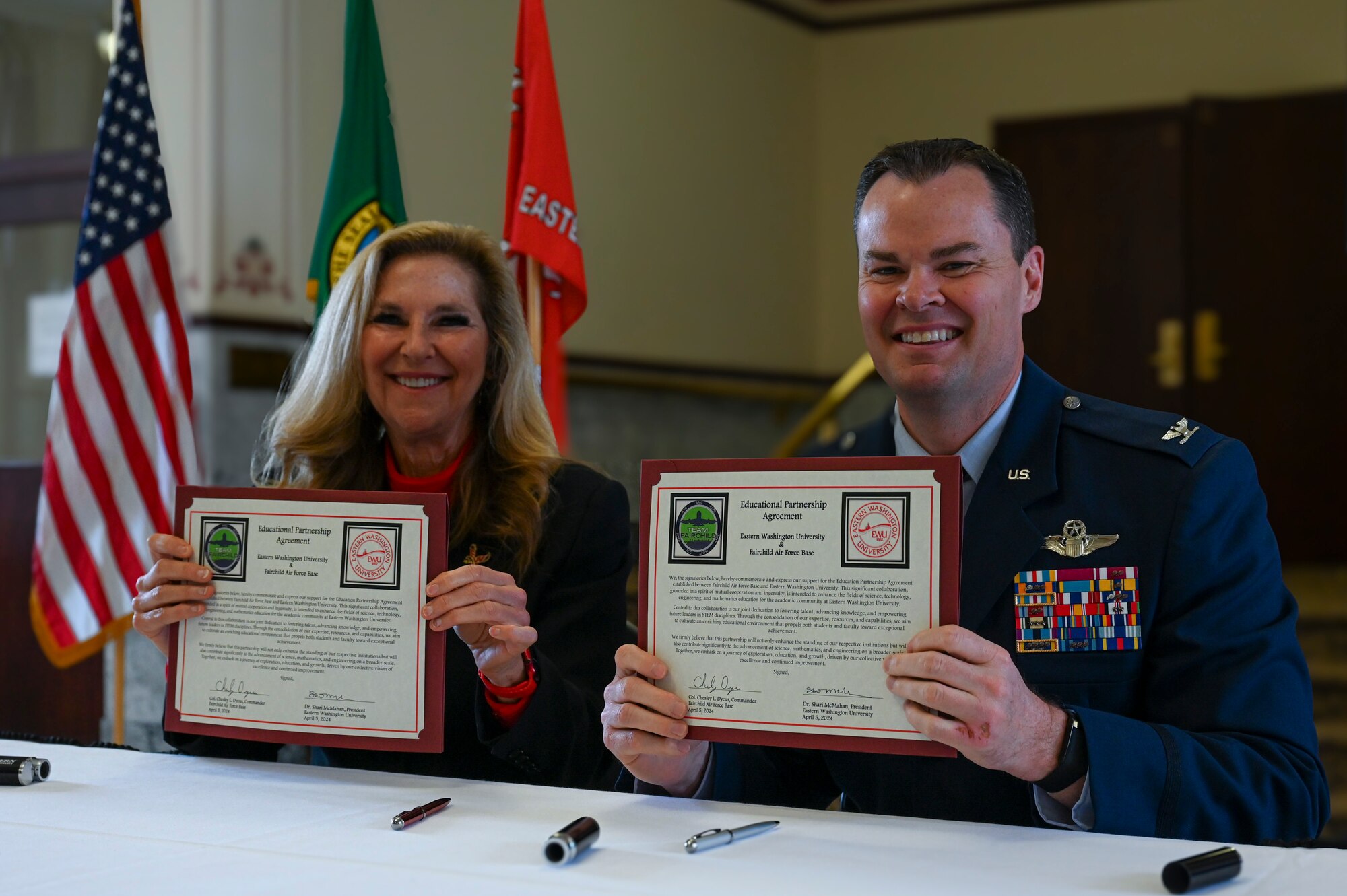 A servicemember and a woman hold up signed documents