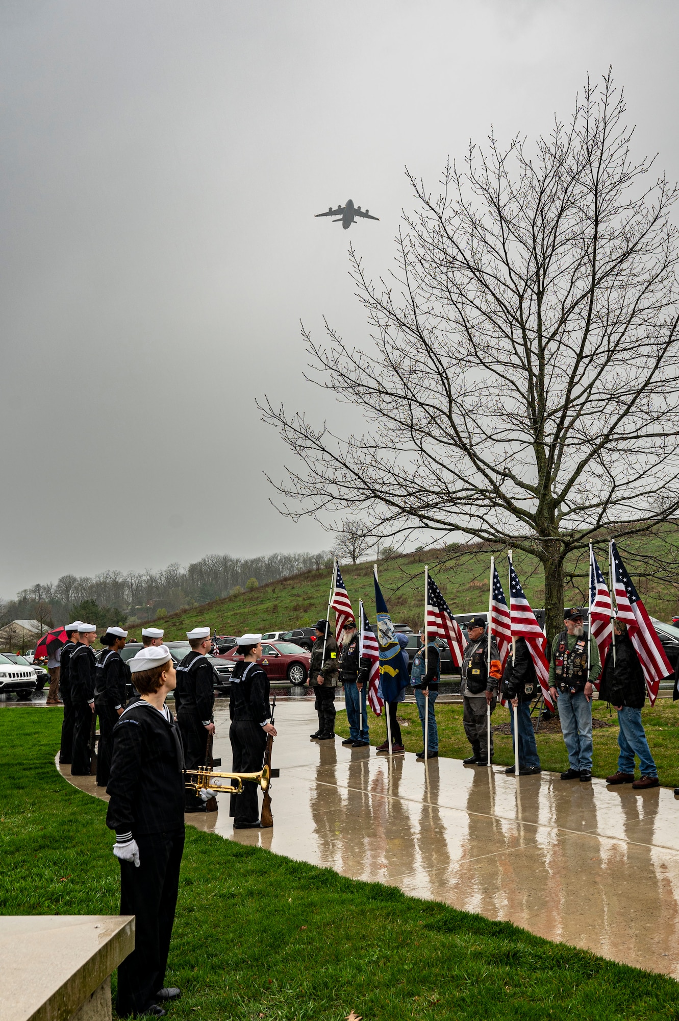 Sailors stand at attention and veterans stand with U.S. flags as a C-17 flies overhead