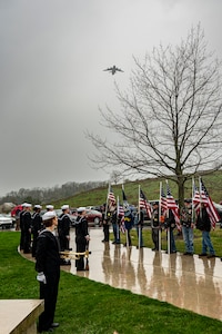 Sailors stand at attention and veterans stand with U.S. flags as a C-17 flies overhead