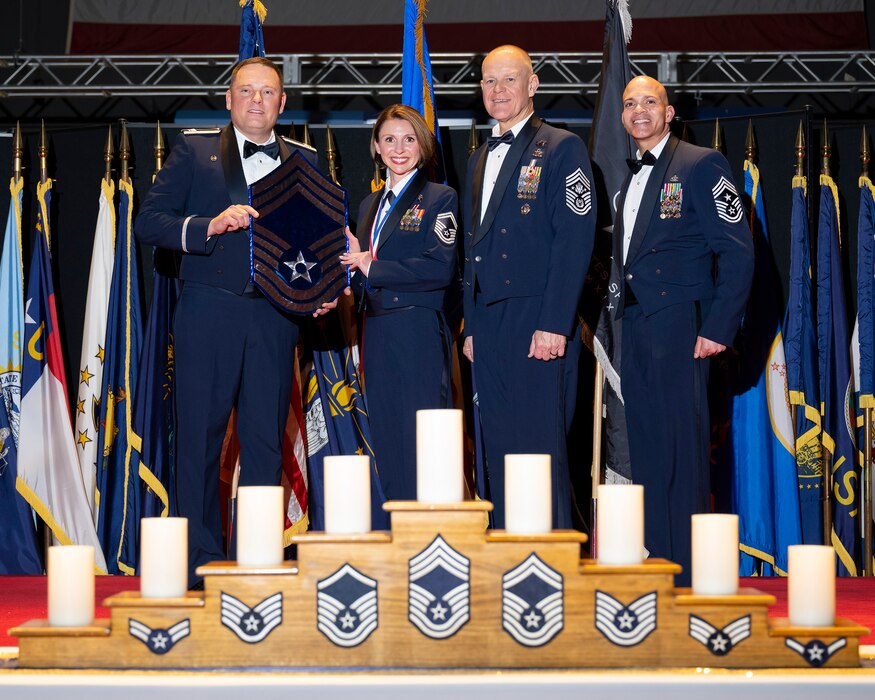 Col. Travis Pond (at left), 88th Air Base Wing and installation commander, presents a memento to Senior Master Sgt. Elise Redziniak, 88th Medical Group, on April 5, 2024, to honor her promotion to the top enlisted rank in the Air Force during the Wright-Patterson Air Force Base, Ohio, chief recognition ceremony at the National Museum of the U.S. Air Force. Retired Chief Master Sgt. of the Air Force James Roy (center) and Chief Master Sgt. Lloyd Morales, 88 ABW command chief, joined the presentation on stage. (U.S. Air Force photo by R.J. Oriez)