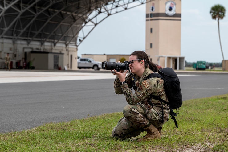 A U.S. Airman kneels holding a camera