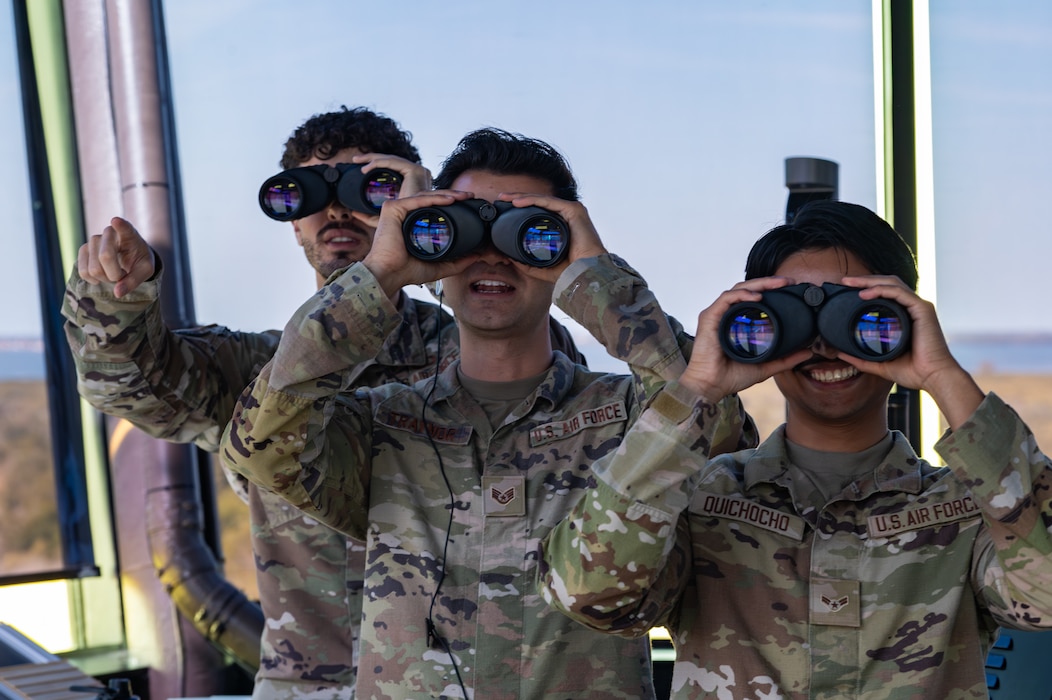 (From left) U.S. Air Force Senior Airman Jantzen Scott, 6th Operation Support Squadron air traffic control trainer, Staff Sgt. Christian Traynor, a 6th OSS ATC watch supervisor, and Airman 1st Class Raymond Quichocho Jr, a 6th OSS ATC apprentice,  look at the flightline through binoculars at MacDill Air Force Base, Florida, April. 8, 2024.