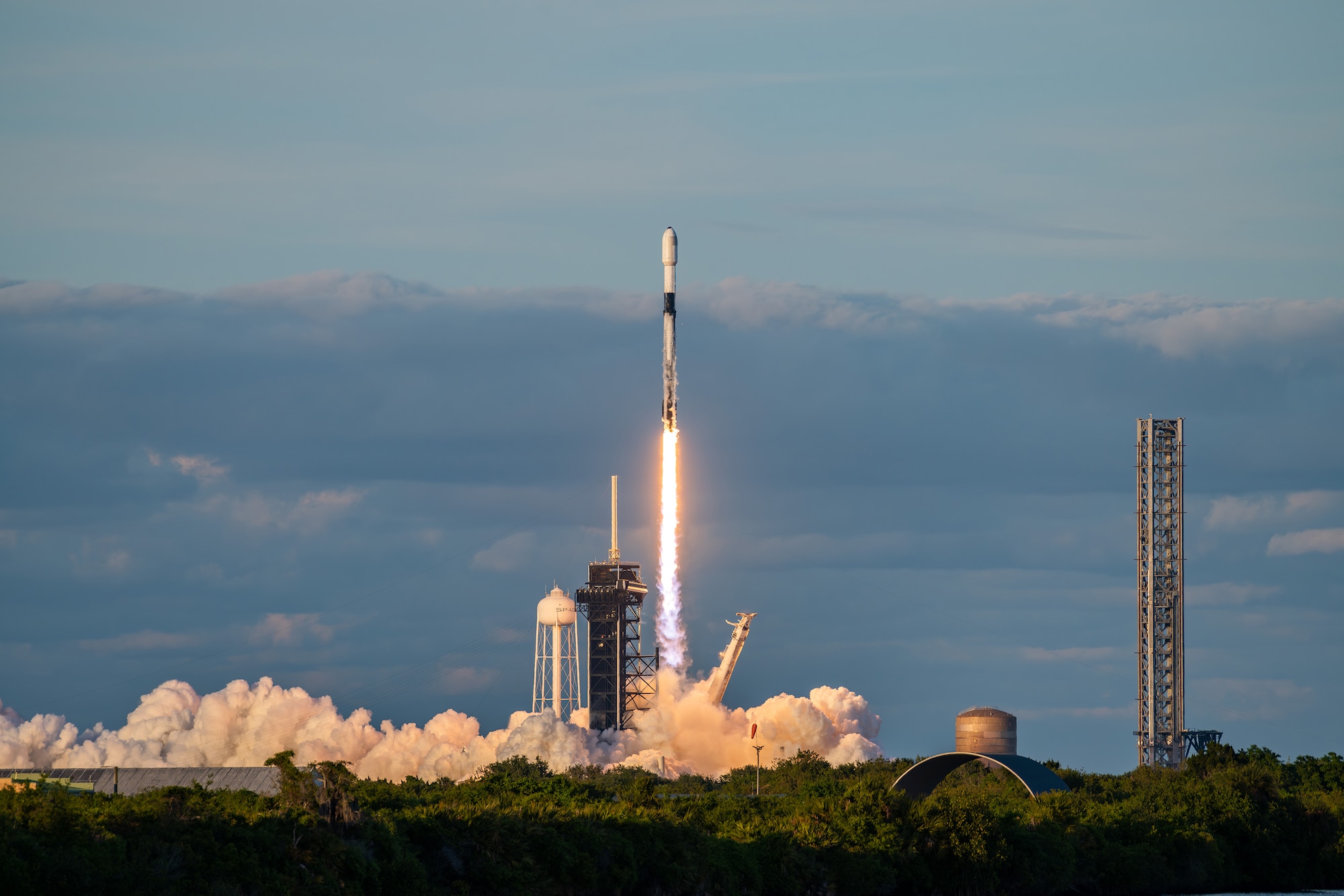 A rocket launches from a platform during daylight, creating white smoke.