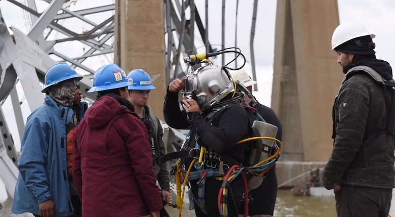 Five people help a salvage diver prepare for a dive