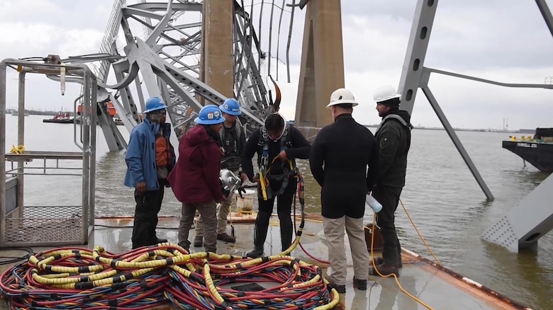 Five people help a salvage diver prepare for a dive