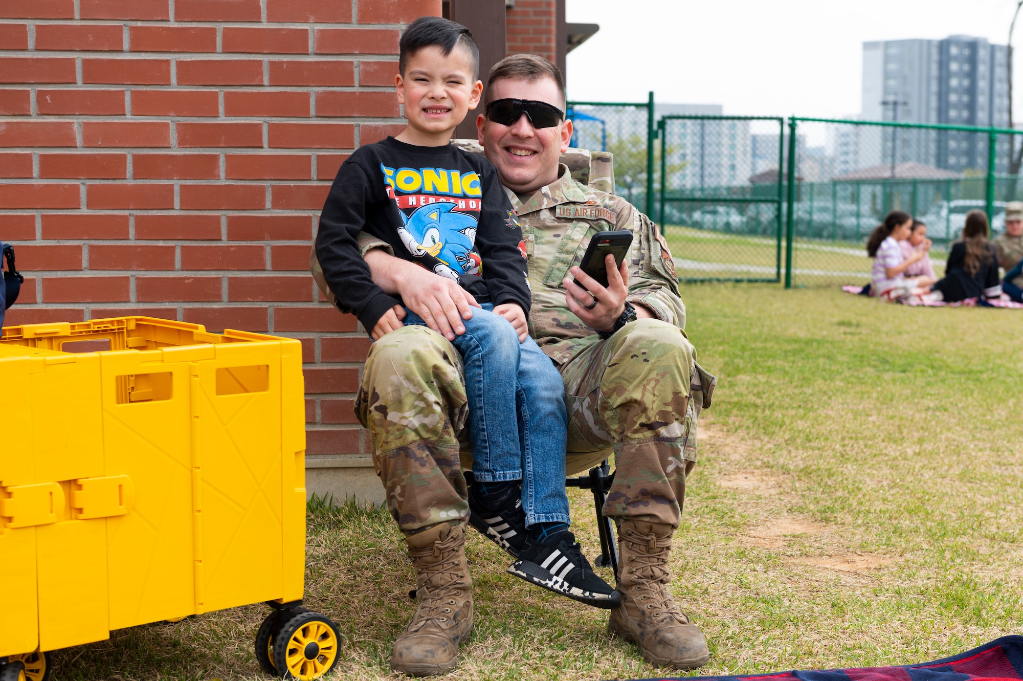 U.S. Air Force Staff Sgt. Taylor McCall, 51st Logistics Readiness Squadron noncommissioned officer in charge of fuels lab, sits in a chair with his child during a Month of the Military Child picnic at Osan Air Base, Republic of Korea, April 10, 2024. MotMC serves as a time to pay tribute to the distinctive journeys and sacrifices of children within military families. (U.S. Air Force photo by Senior Airman Kaitlin Frazier)