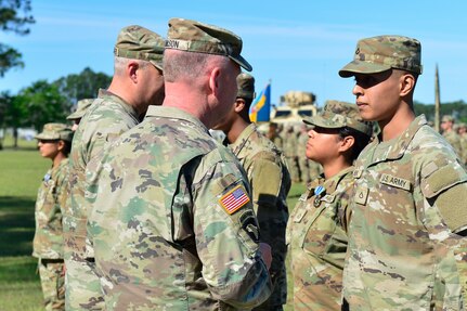 Pfc. Cassandra Vazquez receives an Army Achievement Medal from the Georgia Army National Guard command team of Maj. Gen. Dwayne Wilson and Command Sgt. Maj. John Ballenger during a battle handoff ceremony April 13, 2024, in Fort Stewart, Ga.