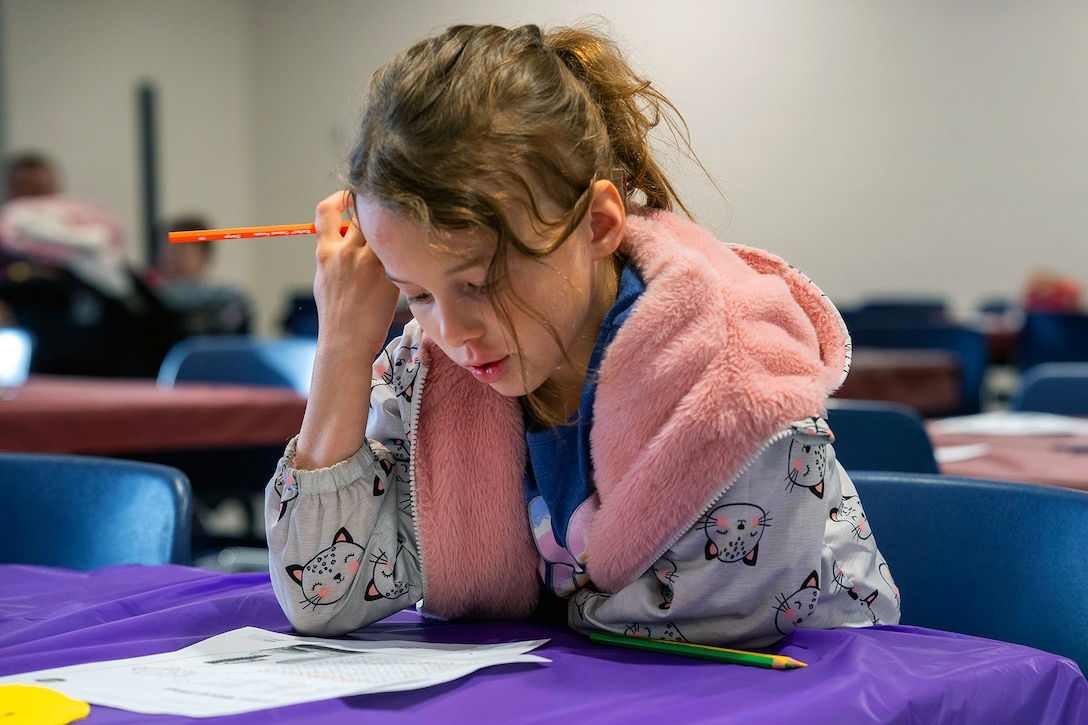 A child sits at a table looking down at a piece of paper.