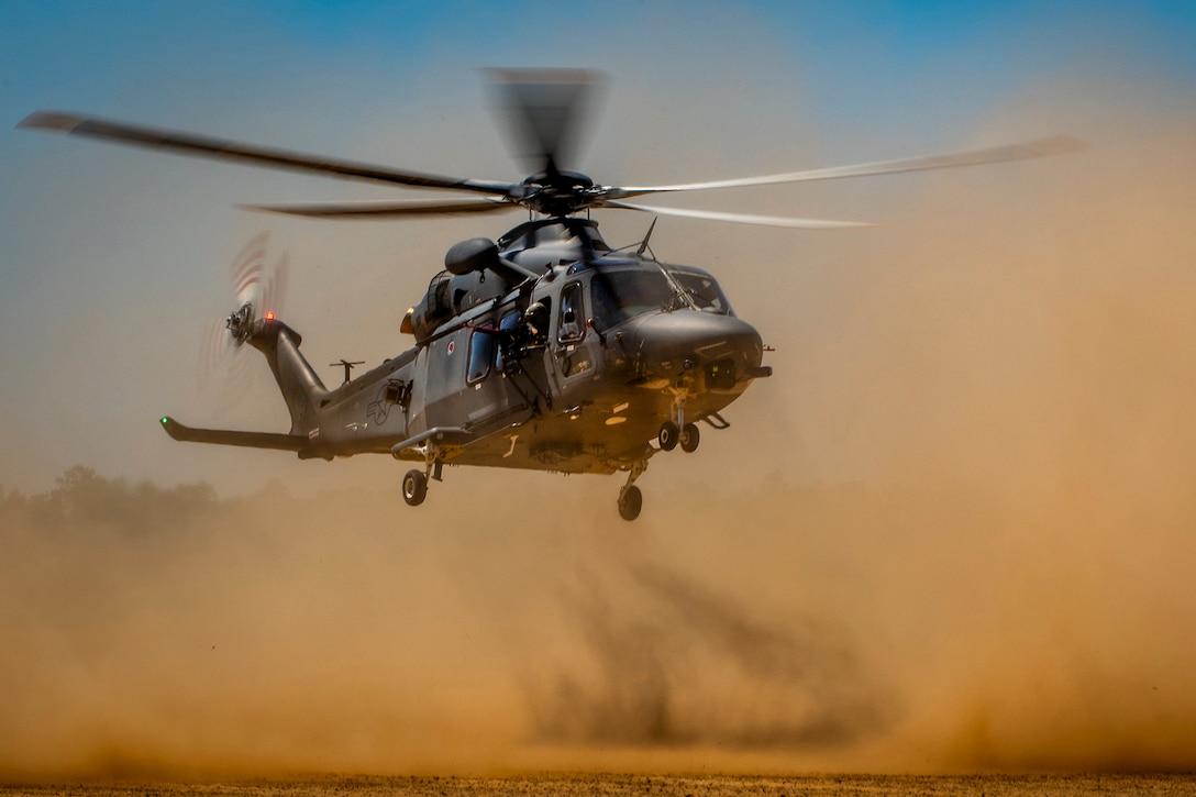 A large helicopter creates a cloud of dust as it lands on a dirt field.