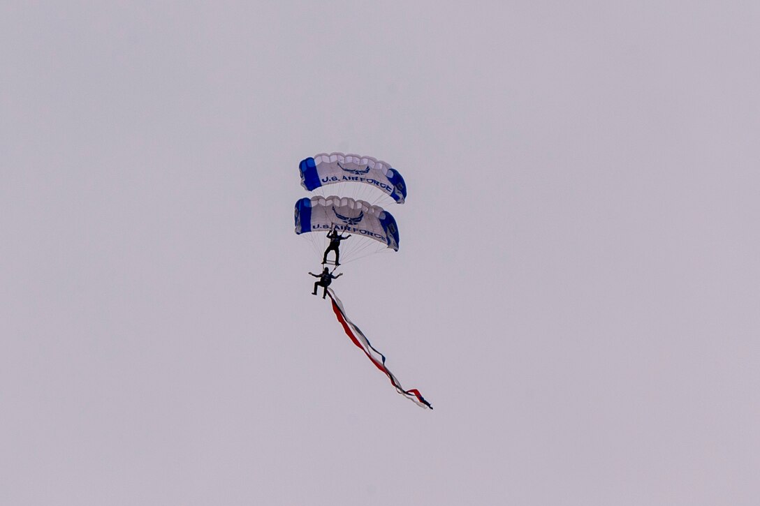 Two service members parachute against a gray sky.