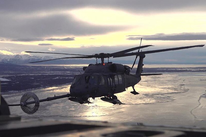 A military aircraft refuels a helicopter over icy waters.