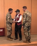 Army Col. Mark Stackle, Brooke Army Medical Center commander, presents Victor Lopez a command coin as BAMC Command Sgt. Maj. John Dobbins looks on during the BAMC Volunteer Recognition Ceremony at Joint Base San Antonio-Fort Sam Houston, Texas, April 5, 2024. Lopez is a 96-year-old Korean and Vietnam war veteran who volunteered at BAMC for more than 29 years after retiring as a sergeant major with 30 years of military service.  (DOD photo by Garron Webster)