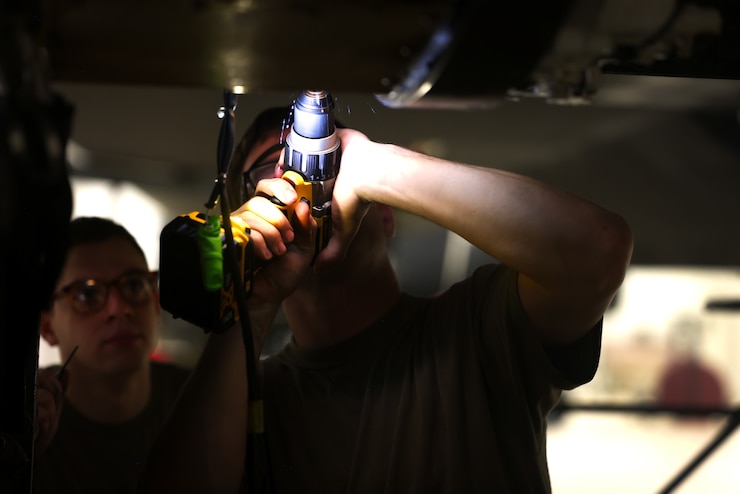 Two U.S. Airmen use a power drill on an aircraft