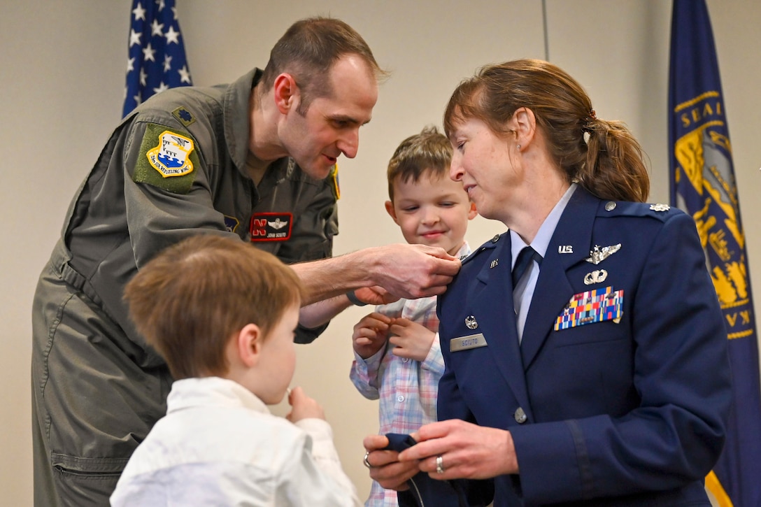 An airman gets a pin on their shoulder by a family member as two children watch.