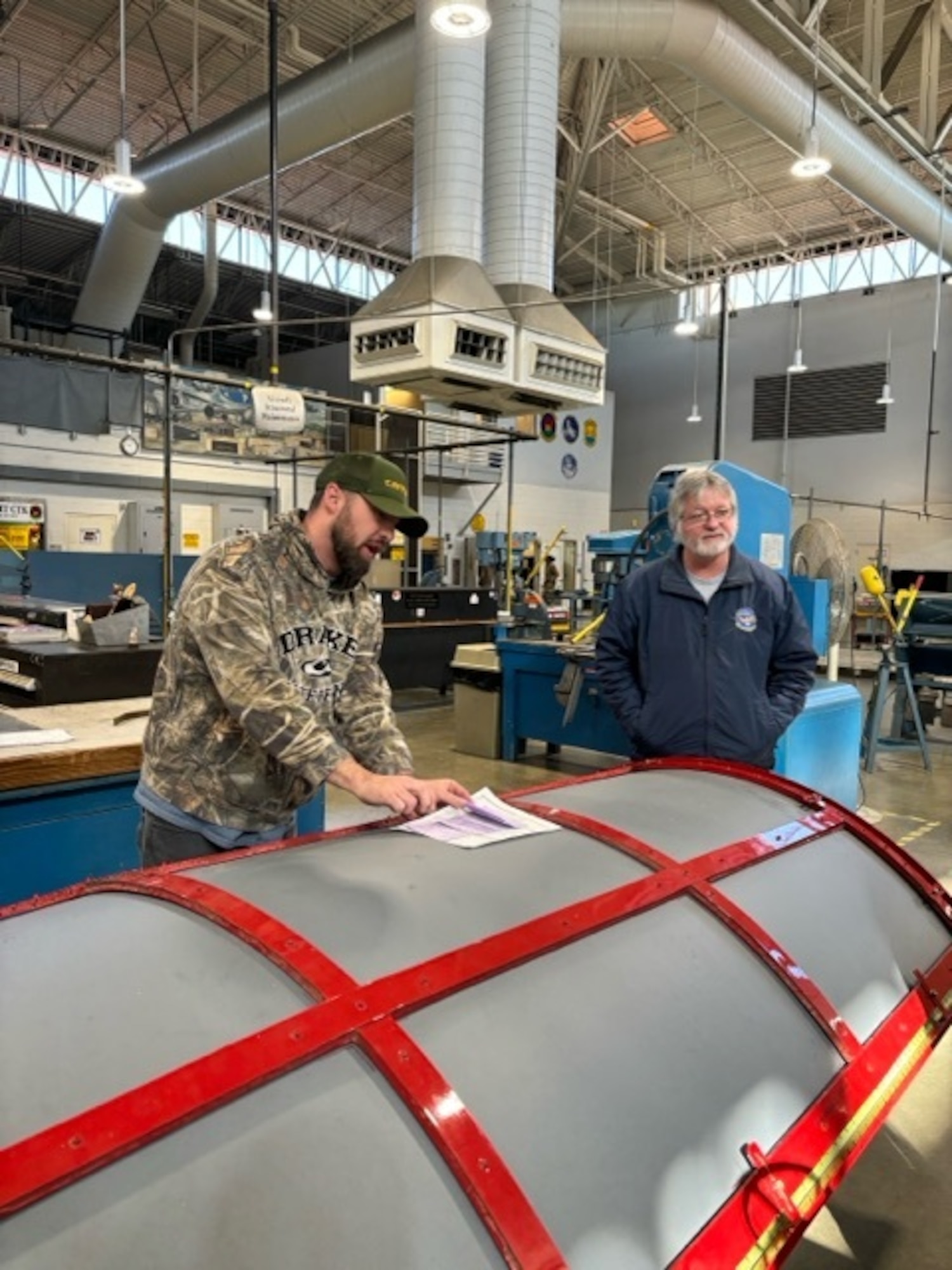 Carson Tyson, 60th Maintenance Squadron (MXS) aircraft structural maintenance technician, signs a form as John Hatchell, 97th MXS Fabrication Flight chief, watches at Travis Air Force Base (AFB), California, April 9, 2024. The personnel at Travis AFB were thankful for the visit from members of the 97th Maintenance Group, and for bringing their knowledge and expertise to their base. (Courtesy photo by Todd Dennison)