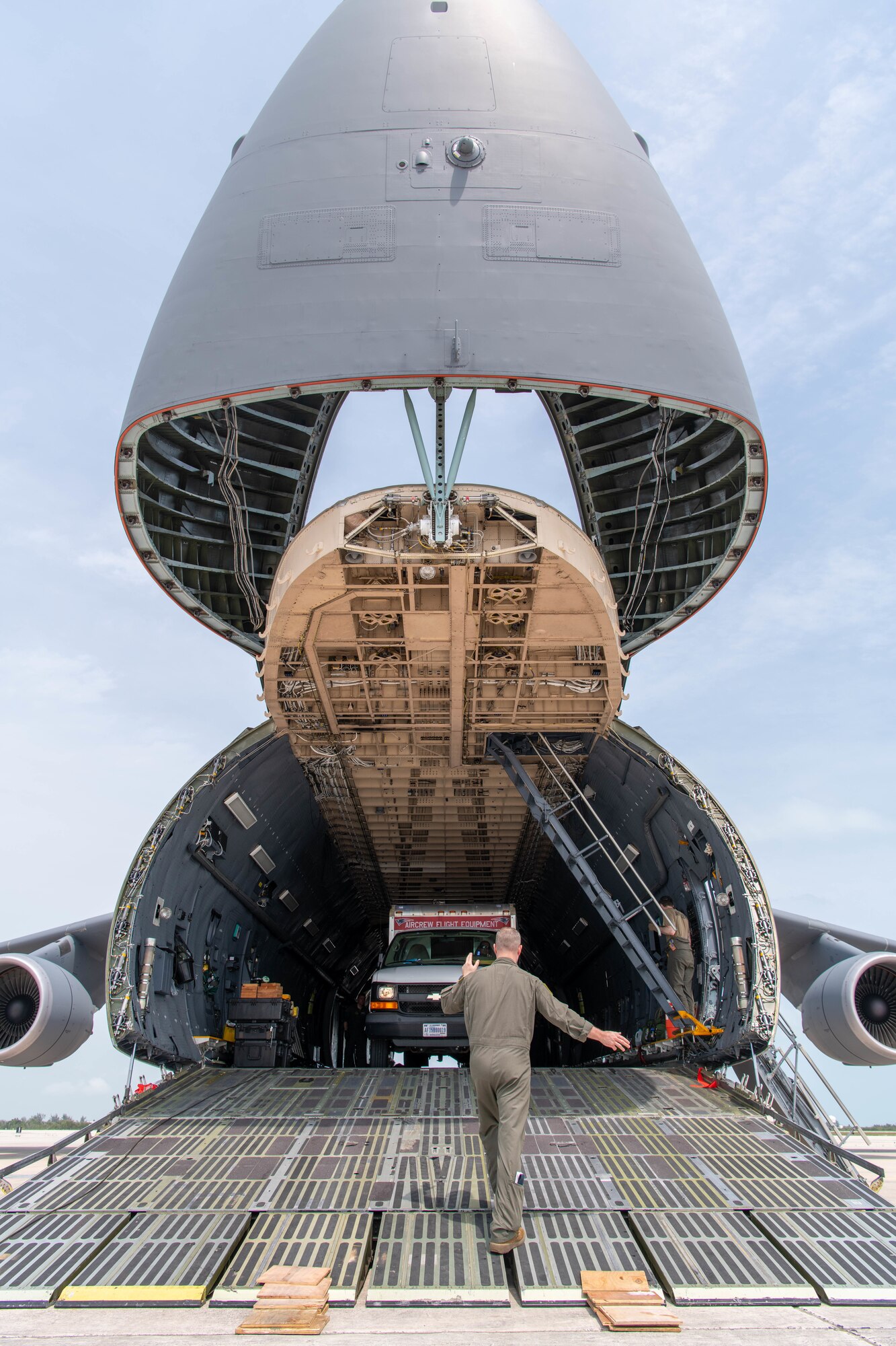 An Airman in uniform with his back to the camera directs a vehicle to be driven off of a C-5M Super Galaxy at Naval Station Key West, Florida.