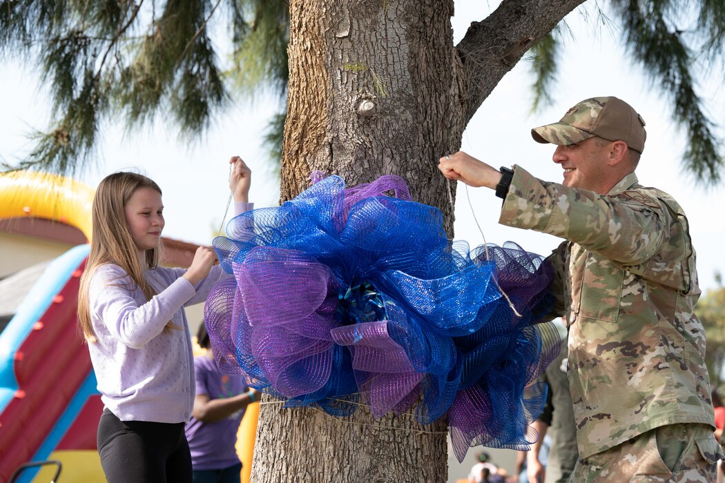 an airman ties a ribbon around a tree with a military child