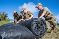 U.S. Air Force Airmen from the 3rd Air Expeditionary Wing out of Joint Base Elmendorf-Richardson, Alaska, roll an expeditionary tent during Exercise Agile Reaper 24-1 at Tinian Forward Operating Site, Northern Mariana Islands, April 8, 2024. Tinian FOS is an austere environment next to Tinian International Airport, and while it began as a barren patch of grass, in less than 24 hours, a few dozen Airmen stood up and began operating it as a fully mission-capable forward operating site comprised of approximately 100 Airmen with all the necessary military support functions to service and launch military aircraft, namely JBER’s F-22 Raptors from the 90th Fighter Squadron. (U.S. Air Force photo by Tech. Sgt. Curt Beach)