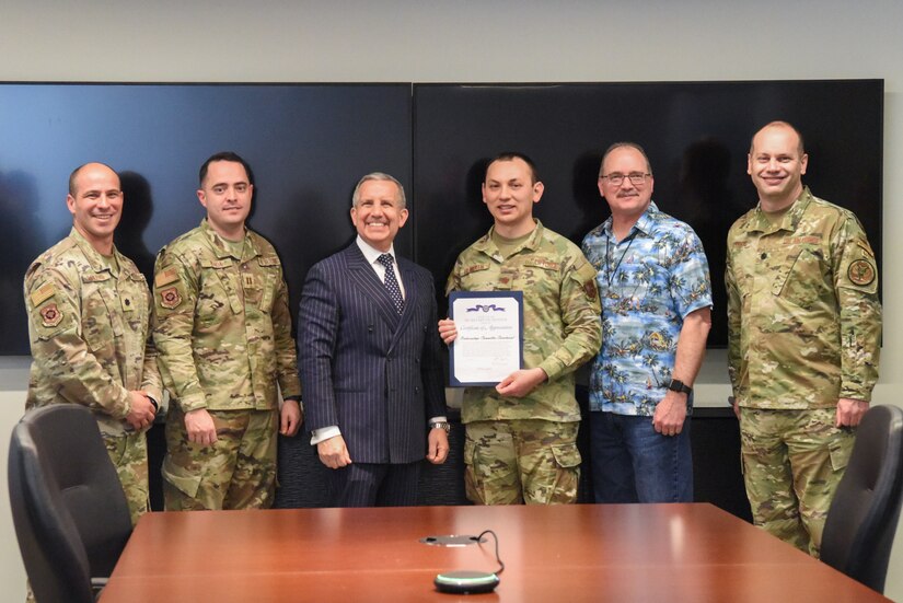 Four service members and two civilians stand for a photo, one displaying a certificate.