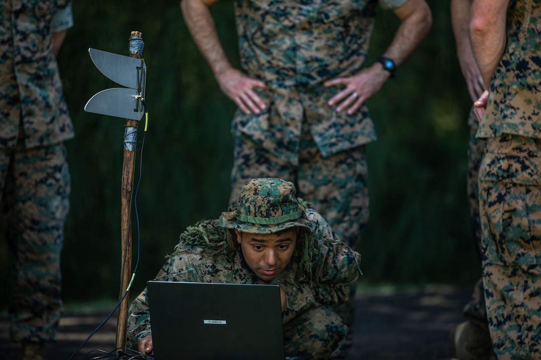 U.S. Marine Corps Lance Cpl. Angel Garcia, an electronic signals intelligence analyst with 3rd Radio Battalion, III Marine Expeditionary Force Information Group, showcases capabilities to III MIG leadership next to a field expedient antenna during a signal's intelligence operation at Camp H.M. Smith, Hawaii on April 9, 2024. The rehearsal trained Marines to collect simulated enemy electronic signals while reducing their own during exercise Corvus Dawn 24 battalion operations. CD24 sharpened 3rd RADBN's ability to provide technical information related capabilities to III Marine Expeditionary Force and the joint and multi-national force throughout the Indo-Pacific region. Garcia is a native of California. (U.S. Marine Corps photo by Staff Sgt. Samuel Ruiz)