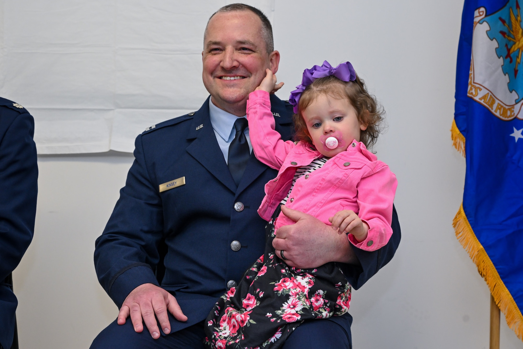 Capt. Jeffrey Kinsey, 910th Logistics Readiness Squadron commander, listens to opening remarks during the assumption of command ceremony while holding his daughter at Youngstown Air Reserve Station, Ohio, April 6, 2024.