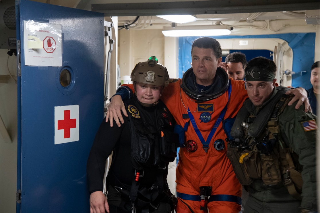 U.S. Navy Hospital Corpsman 2nd Class Jonathan Lamberth from Fayetteville, North Carolina (left), and Chief Naval Aircrewman (Helicopter) Kevin Adams from Vallejo, California (right), both assigned to Helicopter Sea Combat Squadron 23, assist NASA astronaut U.S. Navy Capt.  Reid Wiseman (center) through the medical facilities aboard of San Antonio-class amphibious transport dock ship USS San Diego (LPD 22) during Underway Recovery Test 11, Feb. 27, 2024. In preparation for NASA’s Artemis II crewed mission, which will send four astronauts in Orion beyond the Moon, NASA and the Department of Defense will conduct a series of tests to demonstrate and evaluate the processes, procedures, and hardware used in recovery operations for crewed lunar missions. The U.S. Navy has many unique capabilities that make it an ideal partner to support NASA, including its amphibious ships with the ability to embark helicopters, launch and recover small boats, three-dimensional air search radar and advanced medical facilities. (U.S. Navy photo by Mass Communication Specialist 1st Class Brandon Woods)
