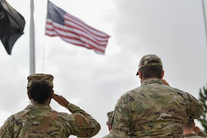 Two uniformed military members are shown saluting a flag.