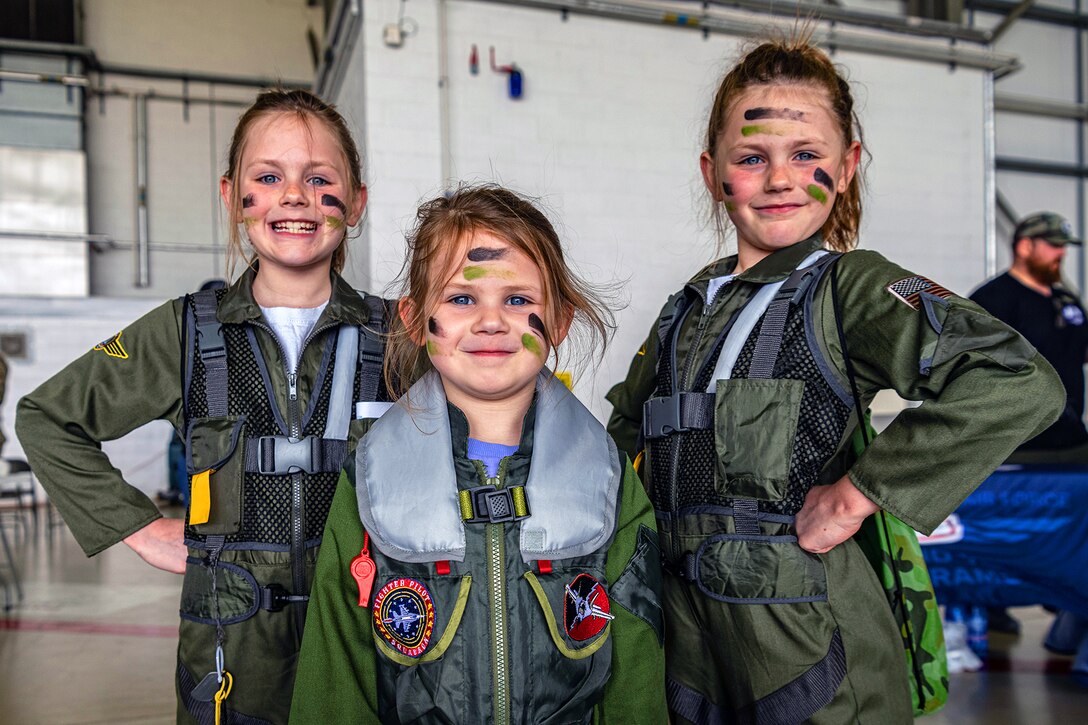 Three children wearing face paint and flight suit-type outfits stand for a photo.