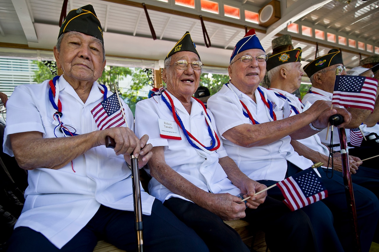 Seated veterans holding small U.S. flags smile.